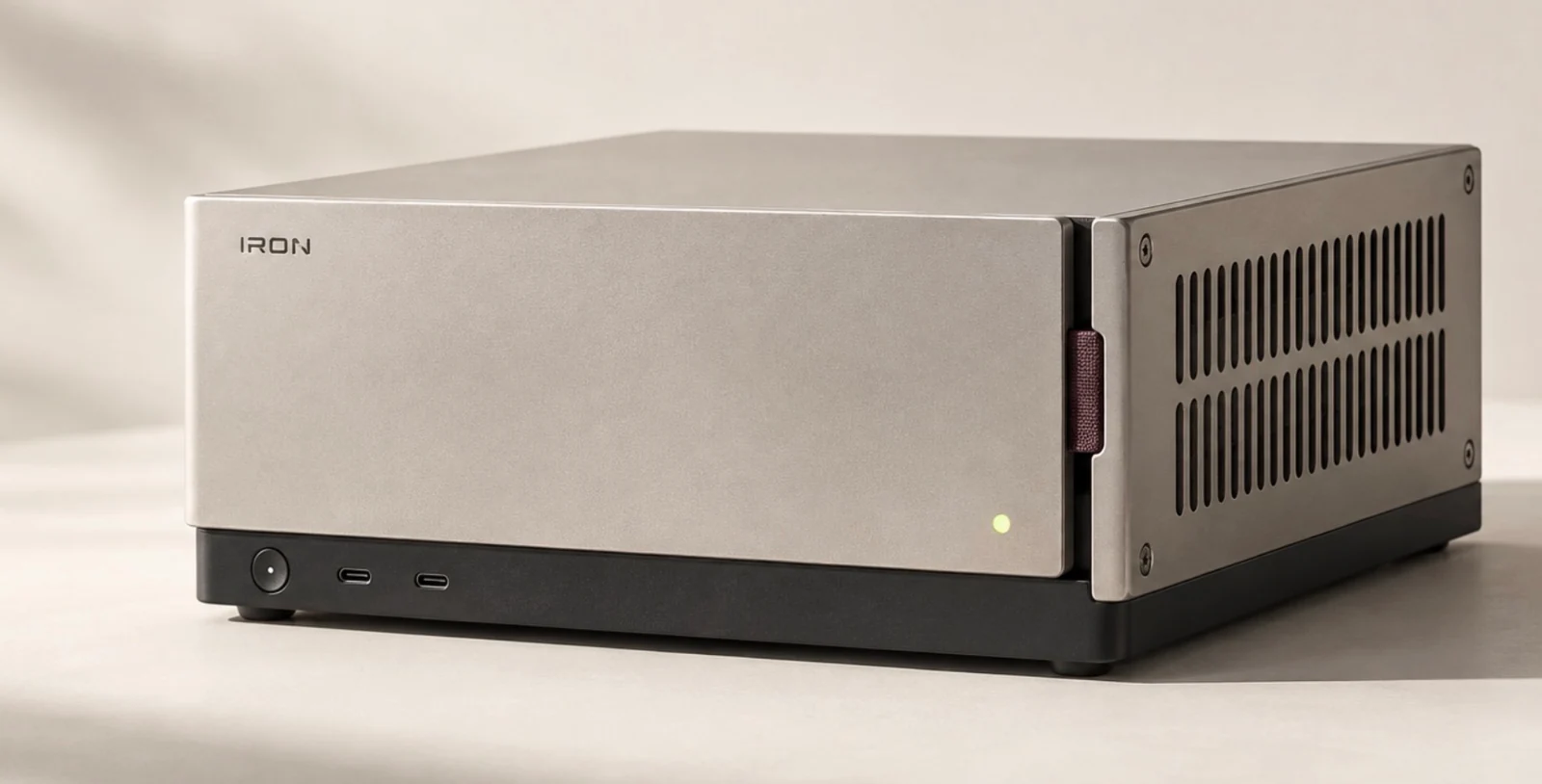 Iron enclosure concept in satin silver, with a graphite base, two front USB-C ports, a plum fabric tab and a vented side panel.